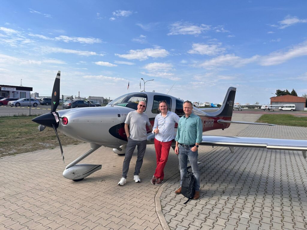 Drei Teilnehmer des geplanten Cirrus-Kaufs vor einer Cirrus SR22 am Flugplatz Prag-Letňany